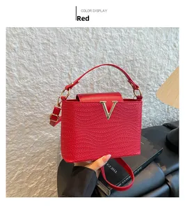 Detail van rode handtas met textuur leer, gouden V-gesp en ronde handgreep
