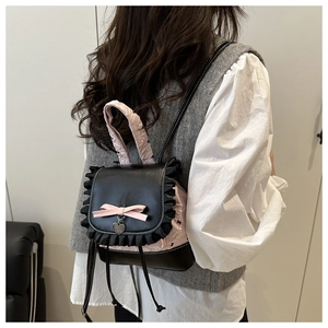 Detailed view of mini black PU backpack with pink lace trim and heart pendant on model