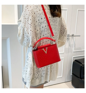 Detail of red woven leather shoulder bag with golden V-shaped buckle on white knitwear