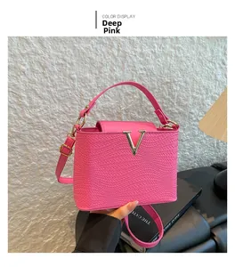 Detail van donkerroze crossbodytas met geweven textuur en gouden V-vormige metalen gesp