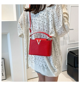 Close-up of a red woven leather crossbody bag with a silver V-shaped buckle on a model