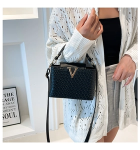 Model wearing a black woven texture crossbody bag with gold V-decoration and thin strap
