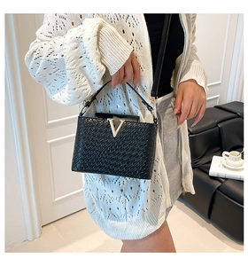 Close-up of black woven bucket bag with golden V buckle and adjustable strap detail