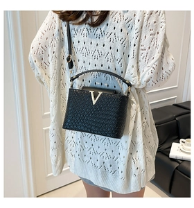 Detail of black faux leather bucket bag with crocodile texture and V-shaped metal clasp
