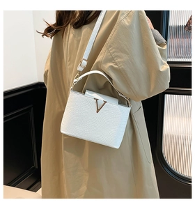 Detail van de witte schoudertas met golftextuur en gouden V-beslag met verstelbare riem