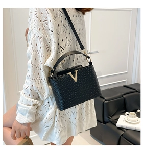 Detail of black woven crossbody bag with gold V-buckle worn by a model in a home setting