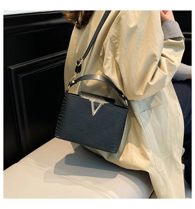 Detail van gestructureerde zwarte crossbodytas met gouden V-sluiting en lederen reliëf