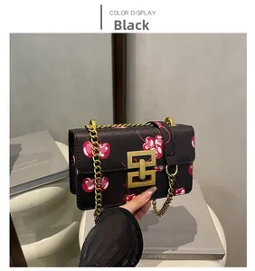 Detail of black cherry print crossbody bag featuring a golden geometric clasp and chain