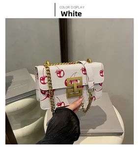 Detail of white litchi grain leather crossbody bag with cherry prints and gold chain strap