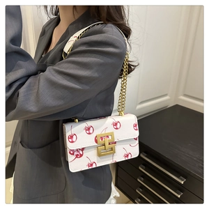 Detail of white leather shoulder bag with red cherry prints and golden metal buckle