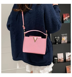 Detail van roze crossbodytas met golvende textuur en gouden V-logo gedragen door model