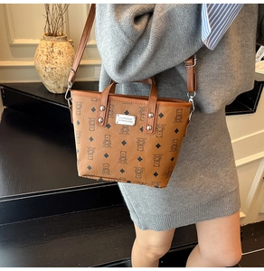 Détail du sac seau marron avec imprimé monogramme ours et plaque logo en métal argenté
