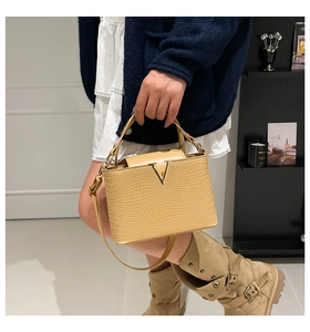 Beige gestructureerde leren trapeze handtas met V-sluiting, gedragen door model