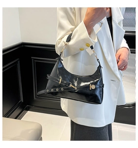 Détail du sac sous le bras en cuir verni noir avec boucle dorée et design de ceinture
