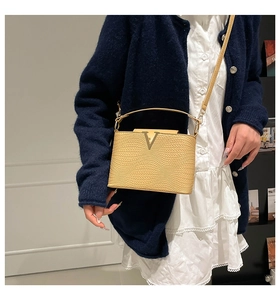 Detail van beige tas met golfstructuur en gouden V-sluiting van gevlochten kunstleer
