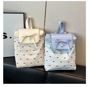 Close-up of bow and pearl charms on textured backpacks with red butterfly patterns