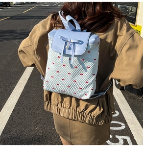 Detail of a floral quilted backpack with blue bow and pearl charm worn by a model outdoors
