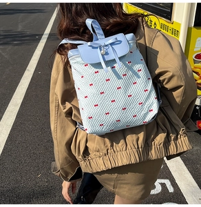 Detailed outdoor view of a light blue lace backpack with red bows and pearl charm