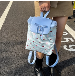 Detail view of light blue backpack with red bow prints and a decorative pearl pendant