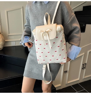 Detail of white backpack with red bow patterns, pearl pendant, and leather strap