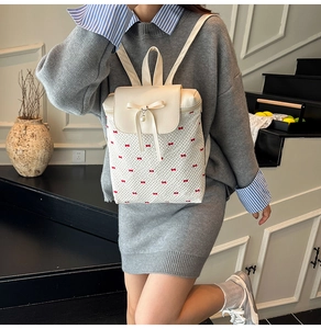 Close-up of beige backpack with red bow print and pearl pendant on a fashion model