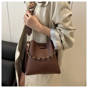Detail of dark brown pebble leather bucket bag with wide woven strap and gold chain handle