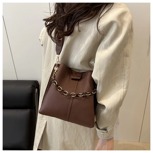 Detail of dark brown pebble leather bucket bag with gold chain and crossbody strap