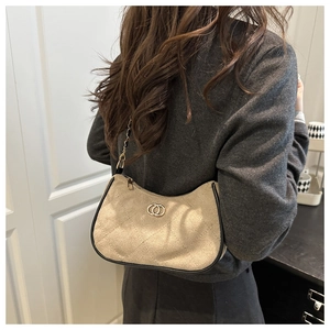 Close-up of quilted suede bag with gold circular logo and elegant black edge piping