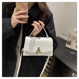 Détail d'un petit sac carré blanc avec boucle dorée porté à la main par un mannequin