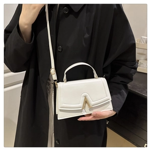 Vue détaillée du mini sac carré blanc avec fermoir en V doré sur un manteau noir élégant