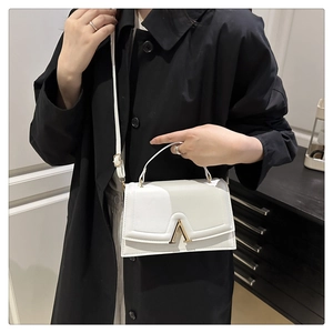 Close-up of a white textured square handbag featuring a gold V-shaped metal lock detail