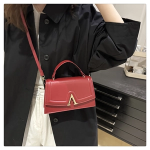 Red crossbody bag with gold V-metal buckle worn with black trench coat and white pants