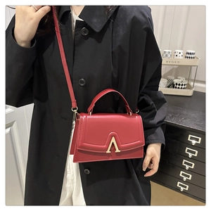 Sac carré rouge avec logo en V doré, porté sur un manteau noir élégant pour femme