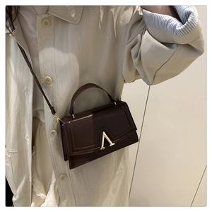 Detail of a dark brown leather square bag featuring a gold V-shaped buckle and strap