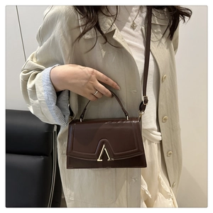 Detail of a brown structured handbag with a gold V-shaped metal clasp and leather strap