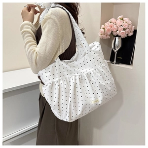 Detail of white polka dot tote bag with pleated ruffles and brand label on nylon surface