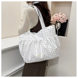 Close-up of white polka dot tote bag with ruffle trim and beige brand woven label