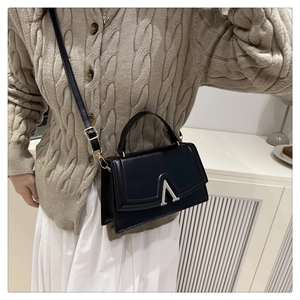 Detail view of a black leather handbag featuring a stylish silver V-shaped buckle closure