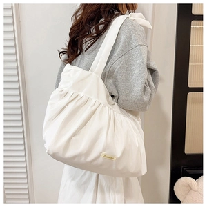 Detail of white pleated tote bag fabric texture with brand label and wide shoulder strap