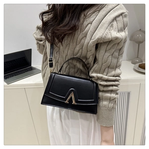 Detail of a black matte faux leather crossbody bag with elegant gold V-shaped metal hardware