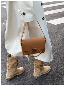 Detail of brown suede shoulder bag with gold chain and metal logo on a white coat
