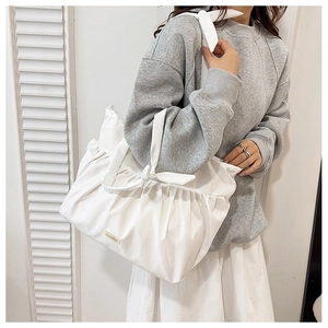 Detail of white pleated shoulder bag featuring a decorative bow knot and golden metal logo