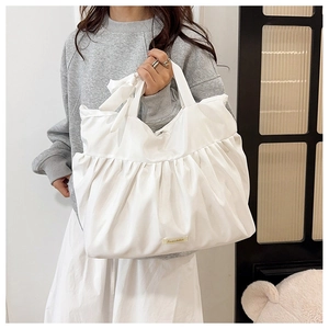 Detailed view of white pleated tote bag featuring decorative bows and logo patch