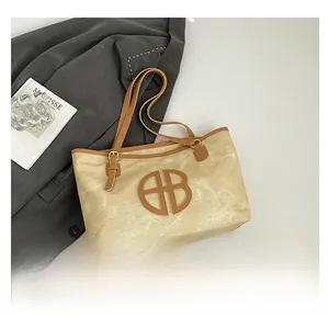 Detail of beige tote bag with brown leather trim and circular cutout logo on front
