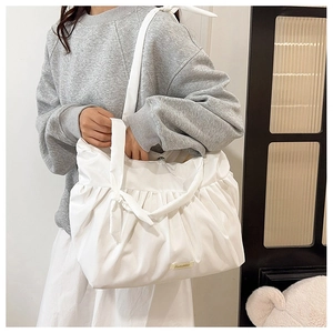 Detail of white pleated nylon tote bag featuring decorative bow shoulder straps