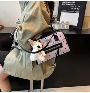 Pink polka dot shoulder bag with cute teddy bear charm shown on a casual trench coat model