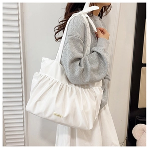 Detail of white pleated tote bag with bow tie strap and brand label on nylon surface
