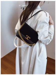 Detail of a black crossbody bag with gold chain strap on a white coat background