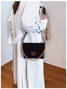 Detail of black flap shoulder bag featuring a gold metal buckle and chunky chain strap