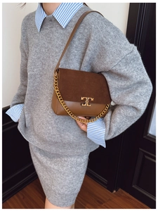 Detail of a brown leather crossbody bag featuring suede flap and gold chain strap